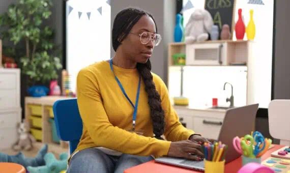 Young teacher working on a laptop in a classroom at a deck featuring one of PowerSchool’s cloud bundles